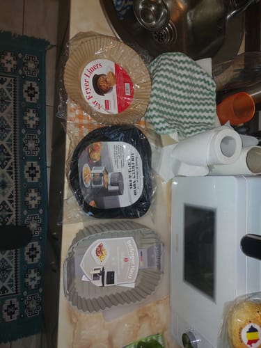 Clientul arată diverse accesorii pentru friteuză, cum ar fi tăvi de hârtie și forme de silicon, în ambalaj.