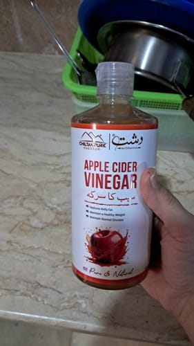 A customer holding a bottle of ChiltanPure Apple Cider Vinegar in their kitchen.