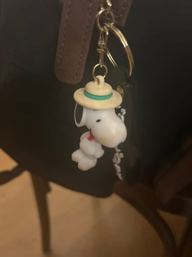 Customer's Straw Hat Snoopy figure keychain attached to the strap of a dark bag.