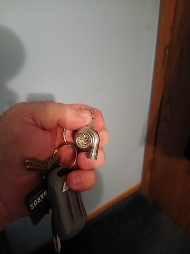 Reviewer holding the metallic TURBO KEYCHAIN attached to a set of keys against a blue wall.