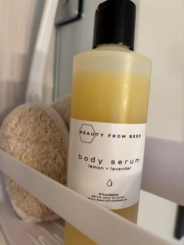 Customer's bottle of lemon and lavender Body Serum resting in a shower caddy next to a loofah.