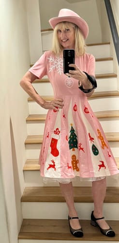 Reviewer taking a selfie on a staircase wearing the Pink 1950s Christmas Snowflake Swing Dress, showing its fit and festive pattern.