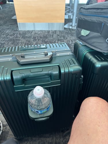 Customer's dark green Carry-On shown in an airport with a water bottle in a holder.