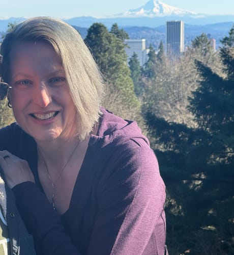 Reviewer smiles while wearing the deep plum Zoey Zip Up Hoodie in a scenic outdoor setting.