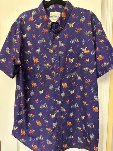 Reviewer's purple Lazer Dinos short sleeve shirt hanging up, showing the all-over print of colorful dinosaurs with lasers.
