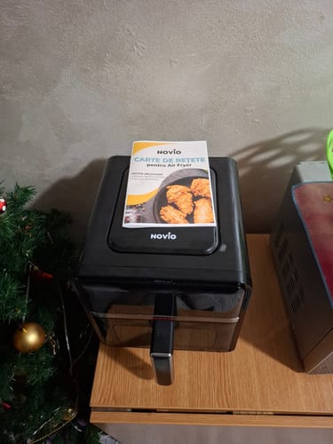 Imaginea clientului cu friteuza Air Fryer Novio StonePro neagră pe un blat de lemn, cu cartea de rețete deasupra.