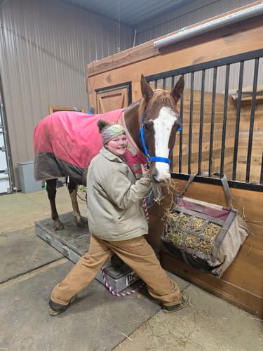 Customer smiling next to their horse Gracie in a stable.