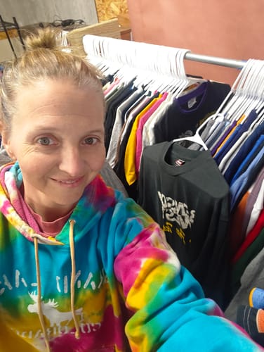 Reviewer in front of a clothing rack filled with numerous t-shirts from their Custom 50lb T-Shirt Bale.