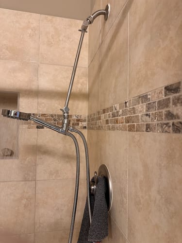 Customer's stainless steel handheld shower head set installed with an extension arm in a tiled shower.