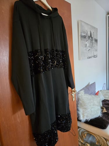 Kundenfoto des schwarzen Kapuzenkleids mit Pailletten-Patchwork, das an einem Kleiderbügel an einer Tür hängt.
