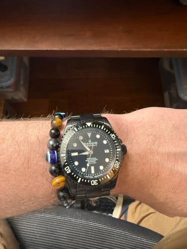 Reviewer wearing the black Oceaneva Deep Marine Explorer II watch on their wrist next to a beaded bracelet.