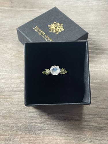 Avis d'un client : la Bague Pierre de Lune et Péridot dans son écrin noir ouvert, montrant la pierre centrale et les péridots.