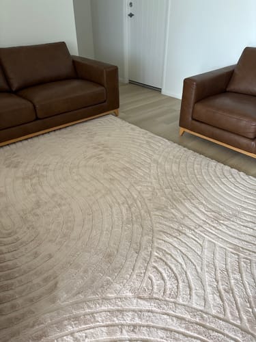 Customer's soft Buttermilk Beige Relax Mat placed on the floor of a living room between two sofas.