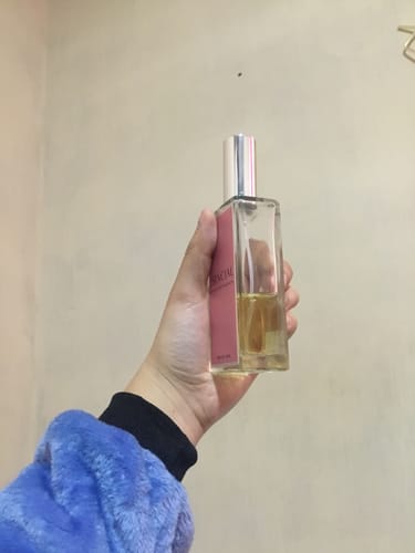 Cliente sosteniendo su botella del perfume M106, que está a la mitad, contra una pared de color neutro.