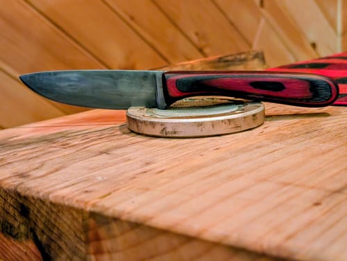 Customer's finished knife with a red and black handle, displayed on a wooden surface after using the sanding belts.