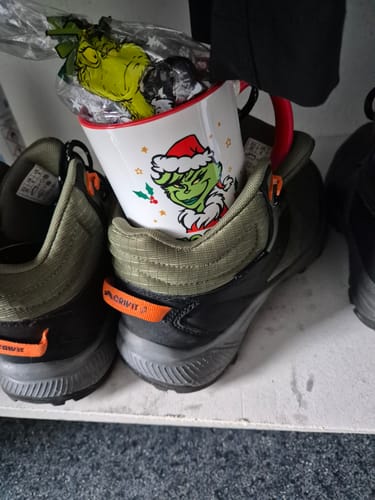 Ein Kunde zeigt die bedruckte Grinch-Tasse, die als Nikolausgeschenk mit Süßigkeiten in einem Schuh steckt.