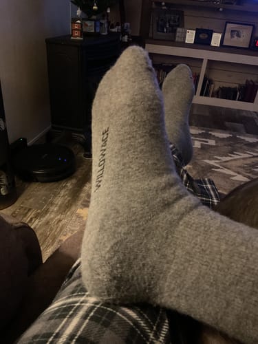 Customer relaxing with their feet up, wearing comfortable grey Men's Alpaca Socks in a living room.