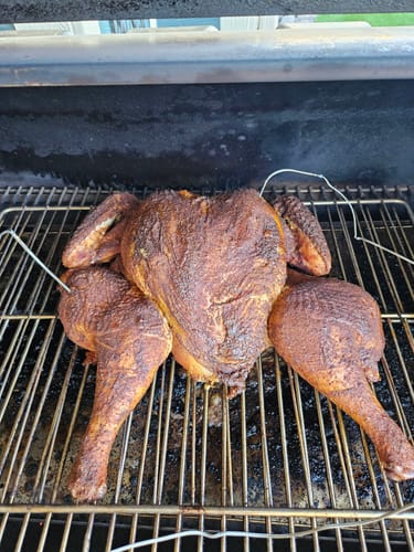 Customer's seasoned, spatchcocked turkey cooking on a smoker grill after using the Turkey Brine Kit.