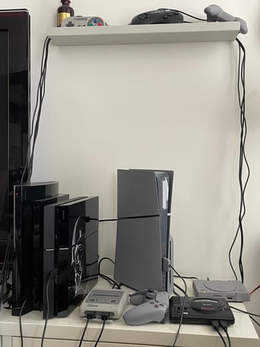 Recensent toont een verzameling spelcomputers die op een witte kast staan opgesteld.