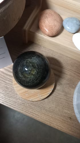 Photo d'un client de la Sphère d'Obsidienne Dorée noire et brillante, posée sur un support en bois sur une table.