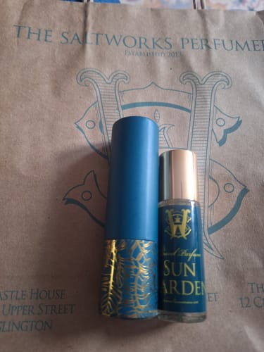Customer's Sun Garden roll-on perfume bottle shown next to its decorative blue and gold case on a branded paper bag.