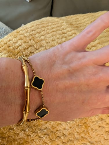 Customer wearing the Celine Clover Bracelet with black enamel charms, layered with another gold bracelet.