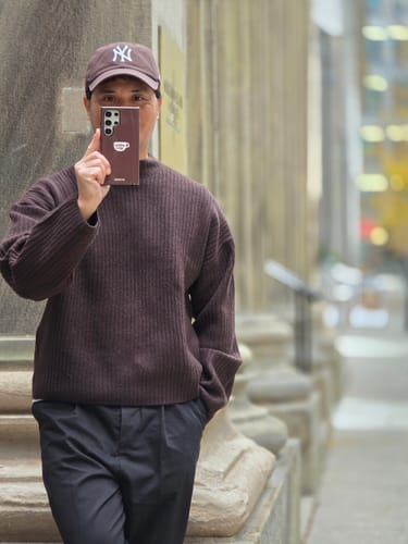 Reviewer holding a phone with a brown KaseMe Impact Case, showing a small coffee cup graphic.