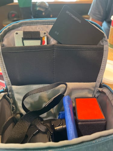 Reviewer's black SPOTMINDERS Tracking Card placed in a pocket inside an open camera bag.