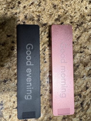 Reviewer's two customized metal Nano Cases, a black 'Good evening' and a pink 'Good morning' case, on a countertop.