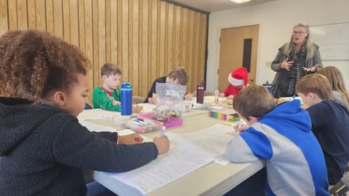 Customer's photo of children in a classroom coloring the USA Map Table Size Coloring Sheets at a table.