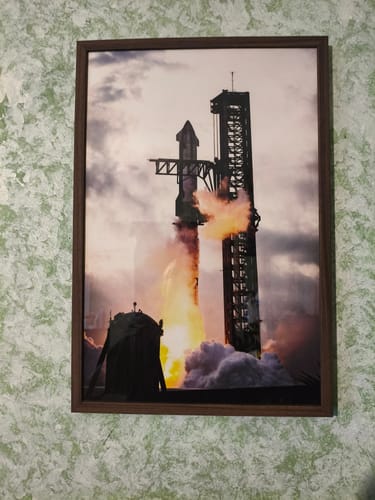 Reviewer's framed IFT3 - Ignition! print with a dark brown frame, hanging on a green patterned wall.