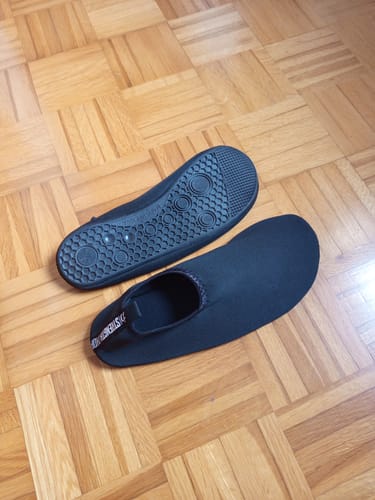Reviewer's black Riot Deadlift Slippers on a wood floor, with one showing the top and one showing the textured sole.