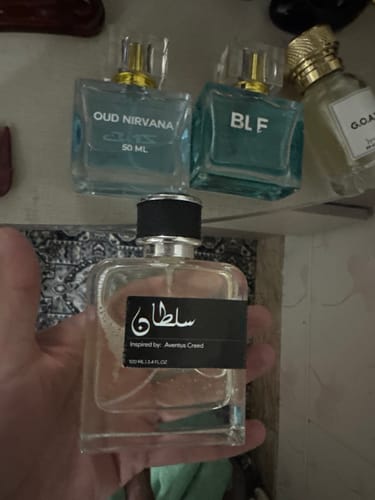Customer holds their clear Sultan perfume bottle, with other fragrances on a shelf in the background.