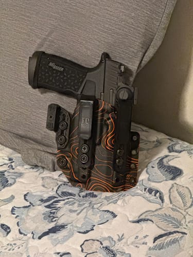 Customer's APX holster in a black and orange topographic pattern, shown tucked into their waistband holding a handgun.