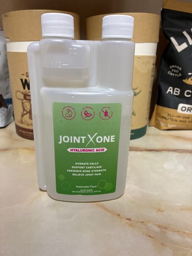 Reviewer's bottle of Joint X One liquid supplement with its unique built-in measuring cup.