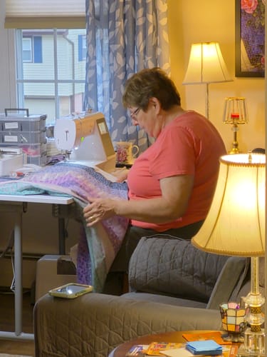 Customer using the Baby Lock Aurora sewing machine to work on a large, colorful quilt in a well-lit room.