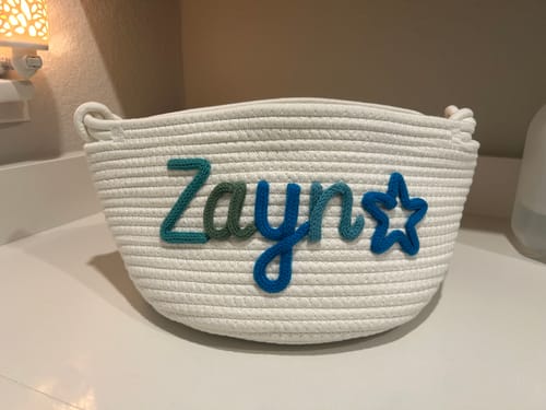 Customer's white Personalized Knitted Basket with the name 'Zayn' and a star icon in multicolor yarn on a countertop.