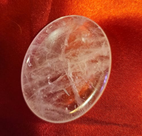 Reviewer's large, smooth quartz crystal from the VIP Crystal Club shown on a red surface.