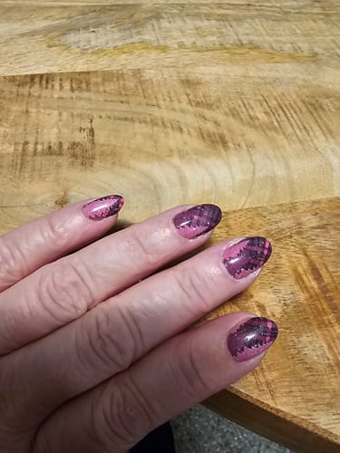 Hand einer Kundin, die die 'Pink Forest Plaid'-Nagelfolien auf mandelförmigen Nägeln aufgetragen hat.