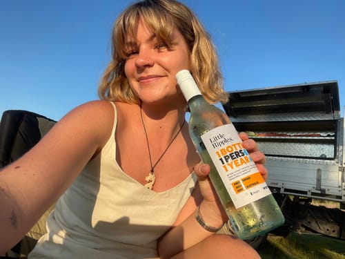 Reviewer smiling outdoors holding a bottle of white wine from the 2025 Chrissy GWP ALL.