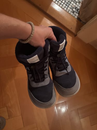 Ein Kunde hält ein Paar der dunkelblauen Kinder Wonderland II Winter-Barfußschuhe.