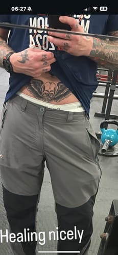 Customer lifts their shirt to show a new winged skull tattoo on their stomach after using the Painless Tattoo Numbing Cream.