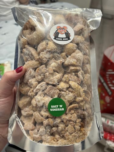 Reviewer holding a large, clear bag of the Triple Seasoning Flavour Boost porkies, showing the Salt 'N Vinegar flavor.