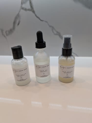 Customer's Anti-Aging Skincare Trio bottles lined up on a white bathroom counter against a marble wall.