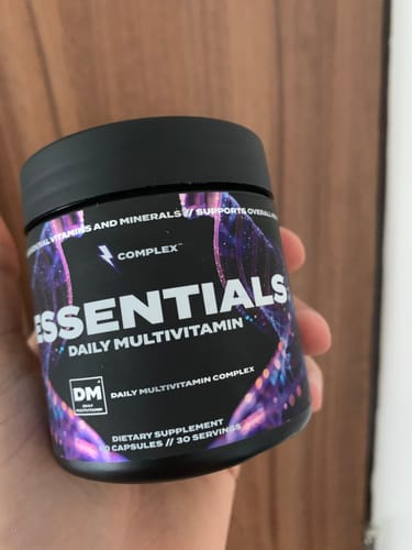 A reviewer holding a black bottle of Complex Essentials Multivitamin in their hand.