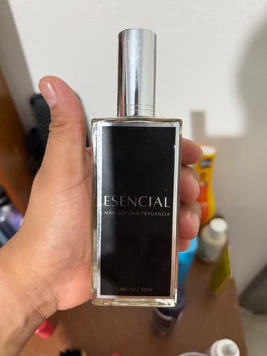 Cliente sosteniendo el frasco de perfume Esencial en la mano, mostrando su etiqueta negra y tapa plateada.