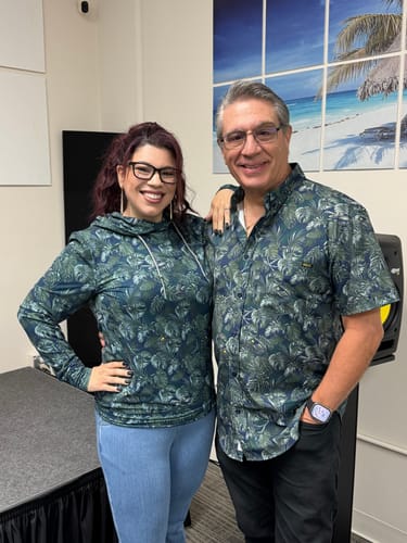 Reviewer wearing the "Clever Girl" Performance Hoodie, standing next to a person in a matching tropical shirt.
