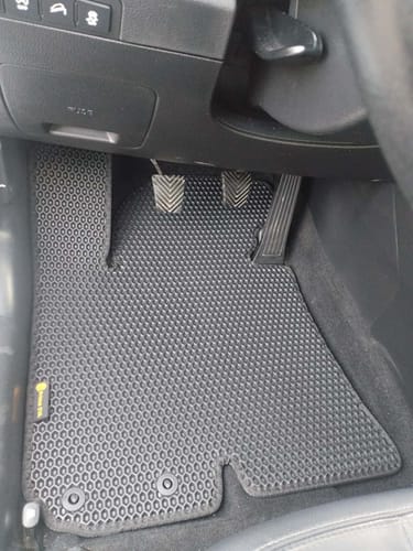 Czarny, dopasowany dywanik samochodowy od klienta, zainstalowany po stronie kierowcy pod pedałami.