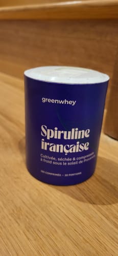 Client montrant le pot bleu de Spiruline Bio Française de la marque Greenwhey sur une surface en bois.