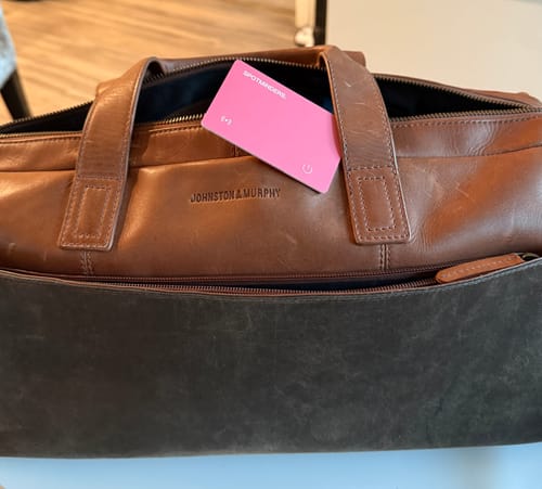 Customer's pink SPOTMINDERS Tracking Card tucked into the pocket of a brown leather bag.